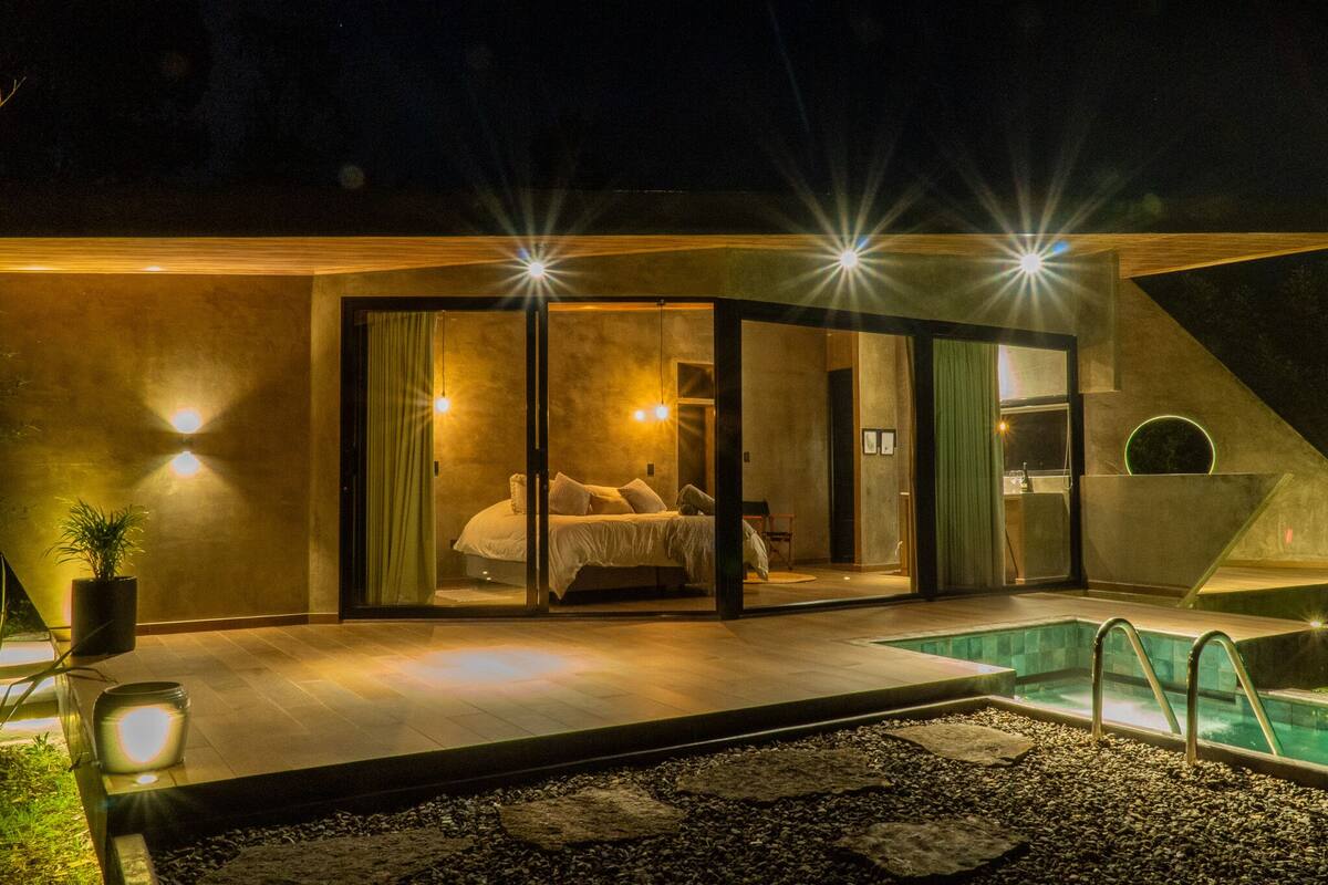 A modern bedroom with a glass door, a pool, and a small outdoor seating area.
