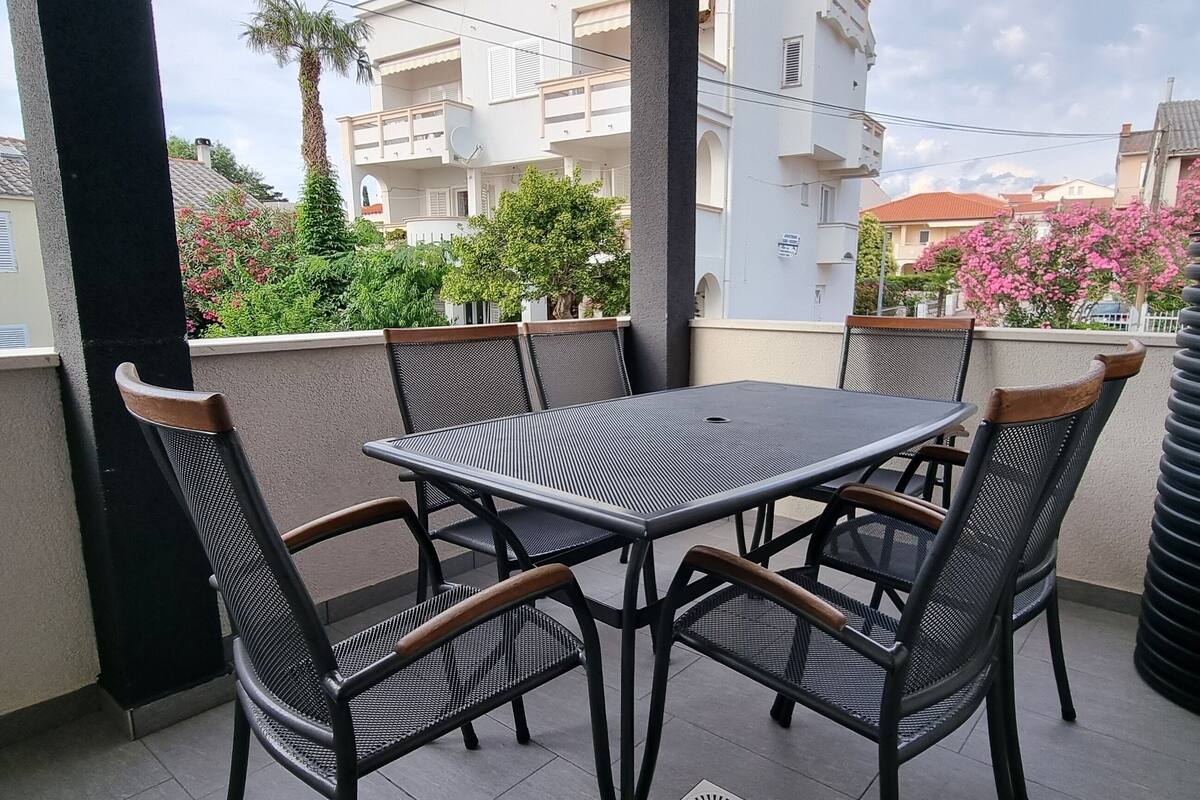 A balcony with a table and chairs, a potted plant, and a view of buildings and trees.