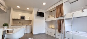 A compact hotel room with a kitchenette, a dining area, and a bunk bed.