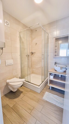 A modern bathroom with a glass-enclosed shower, a white toilet, a sink with a mirror, and wooden flooring.