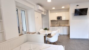 Une cuisine moderne avec des meubles blancs, un four à micro-ondes et un évier. On y trouve un coin repas avec une table et des chaises blanches, ainsi qu'une petite plante en pot posée sur la table.