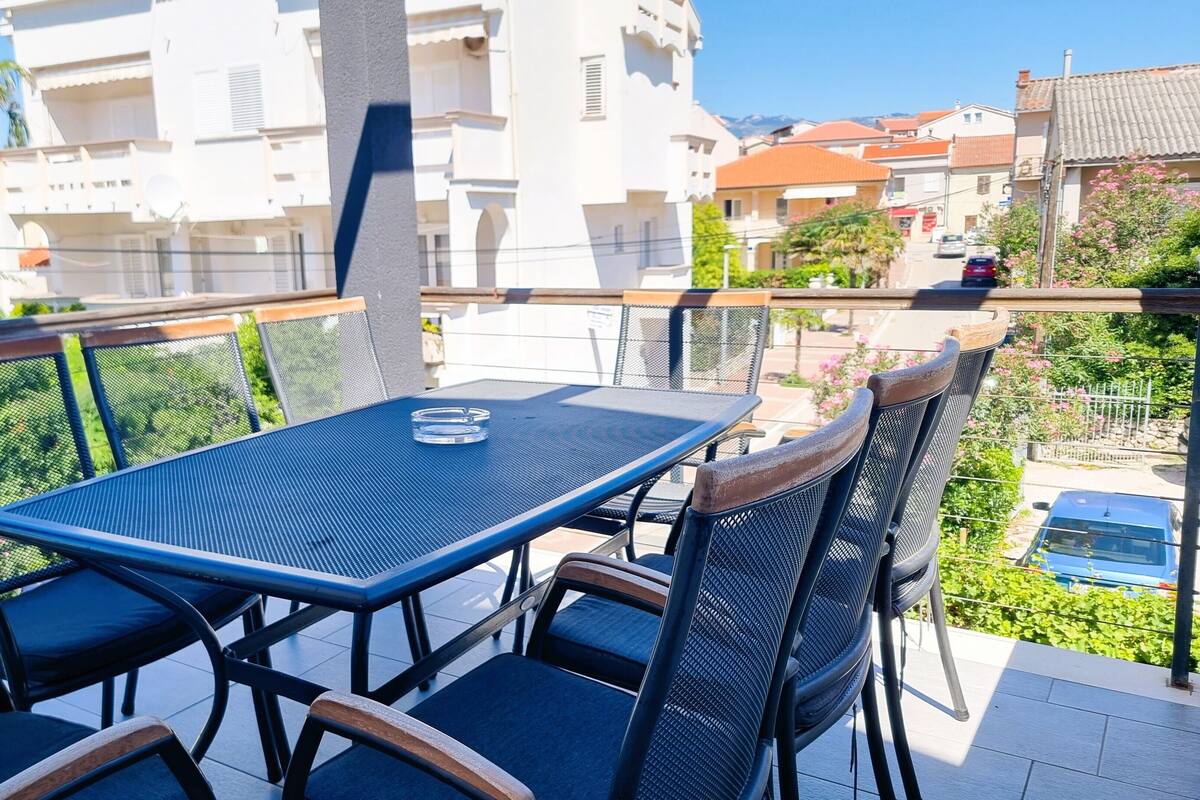 A balcony with a table and chairs, overlooking a residential area with buildings and a clear sky.