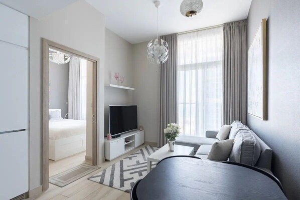 A modern hotel room with a bed, a TV, a sofa, and a large window with curtains.
