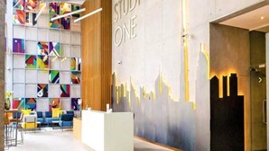 A modern reception area with a colorful geometric wall art, a reception desk, and a seating area with blue and yellow chairs. - Bright 1BR sea view and balcony (Dubai)