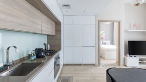 A modern kitchen with a sink, stove, and cabinets, leading to a bedroom with a bed and a TV. - Bright 1BR sea view and balcony (Dubai)