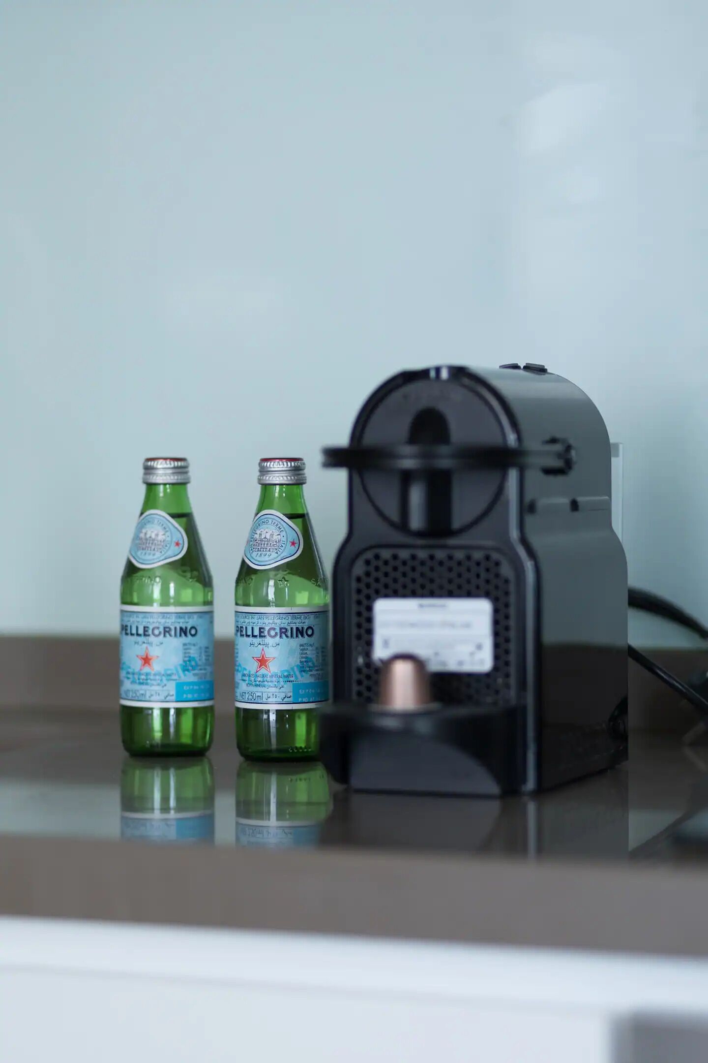 Two Pellegrino water bottles and a coffee machine on a reflective surface.