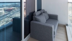 A balcony with a grey sofa and a glass wall offering a city view. - Bright 1BR sea view and balcony (Dubai)