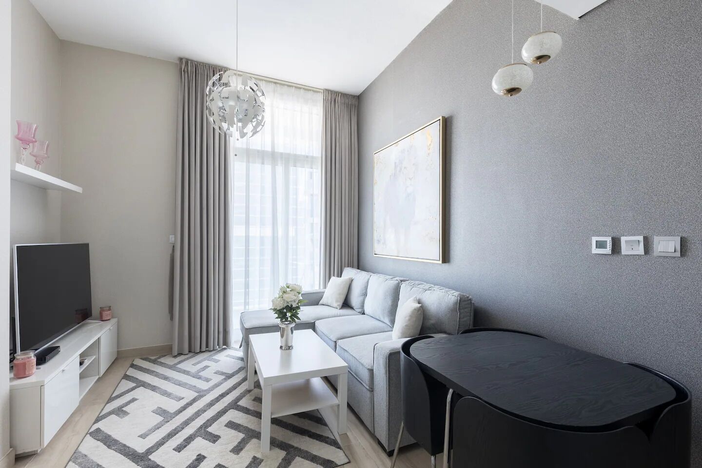 Un salon moderne avec un canapé gris, une table basse blanche, un téléviseur et un coin repas.