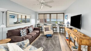 A modern living room with a brown leather sofa, a beige armchair, a wooden coffee table, and a TV on a wooden stand. - Escape to paradise! 1BR Beachfront Condo in Destin (Destin)