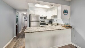 A modern kitchen with white cabinets, a granite countertop, stainless steel appliances, and a built-in oven. - Escape to paradise! 1BR Beachfront Condo in Destin (Destin)