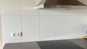 A kitchen with white tiled walls, a stainless steel range hood, and a black induction cooktop. - Ferienwohnung Pfalzblick (Bacharach)