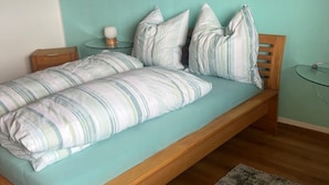 A bed with a striped bedspread and pillows, a wooden headboard, a small bedside table with a lamp, and a glass table with a candle. - Ferienwohnung Pfalzblick (Bacharach)
