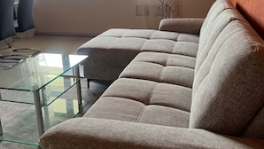 A living room with a sectional sofa, a glass coffee table, and a dining area with chairs. - Ferienwohnung Pfalzblick (Bacharach)