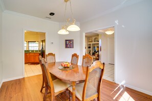 A dining room with a wooden table and chairs, a chandelier, and a view into the kitchen.