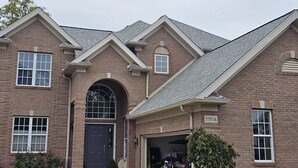 A two-story brick house with a dark front door, a garage, and a small front yard with a tree. - Avon Lake, Avon golf course home, 1,000 s.f. open outdoor deck on course lake (Avon)