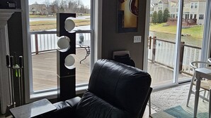 A modern living room with a black leather sofa, a large window, and a view of a residential area. - Avon Lake, Avon golf course home, 1,000 s.f. open outdoor deck on course lake (Avon)