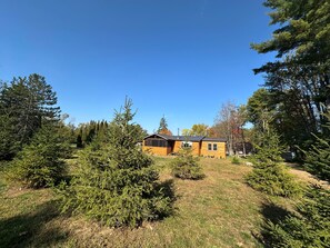 Une cabane avec un toit en pente, entourée d’arbres à feuilles persistantes et bordée d’une pelouse.