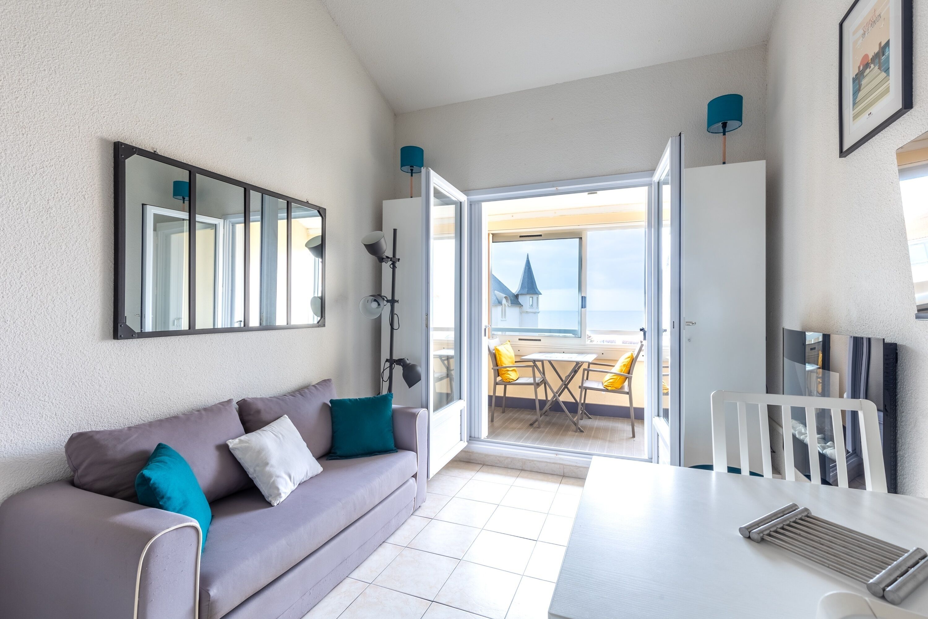 Quarto moderno com sofá, mesa de jantar, TV e uma janela grande com vista para o mar.