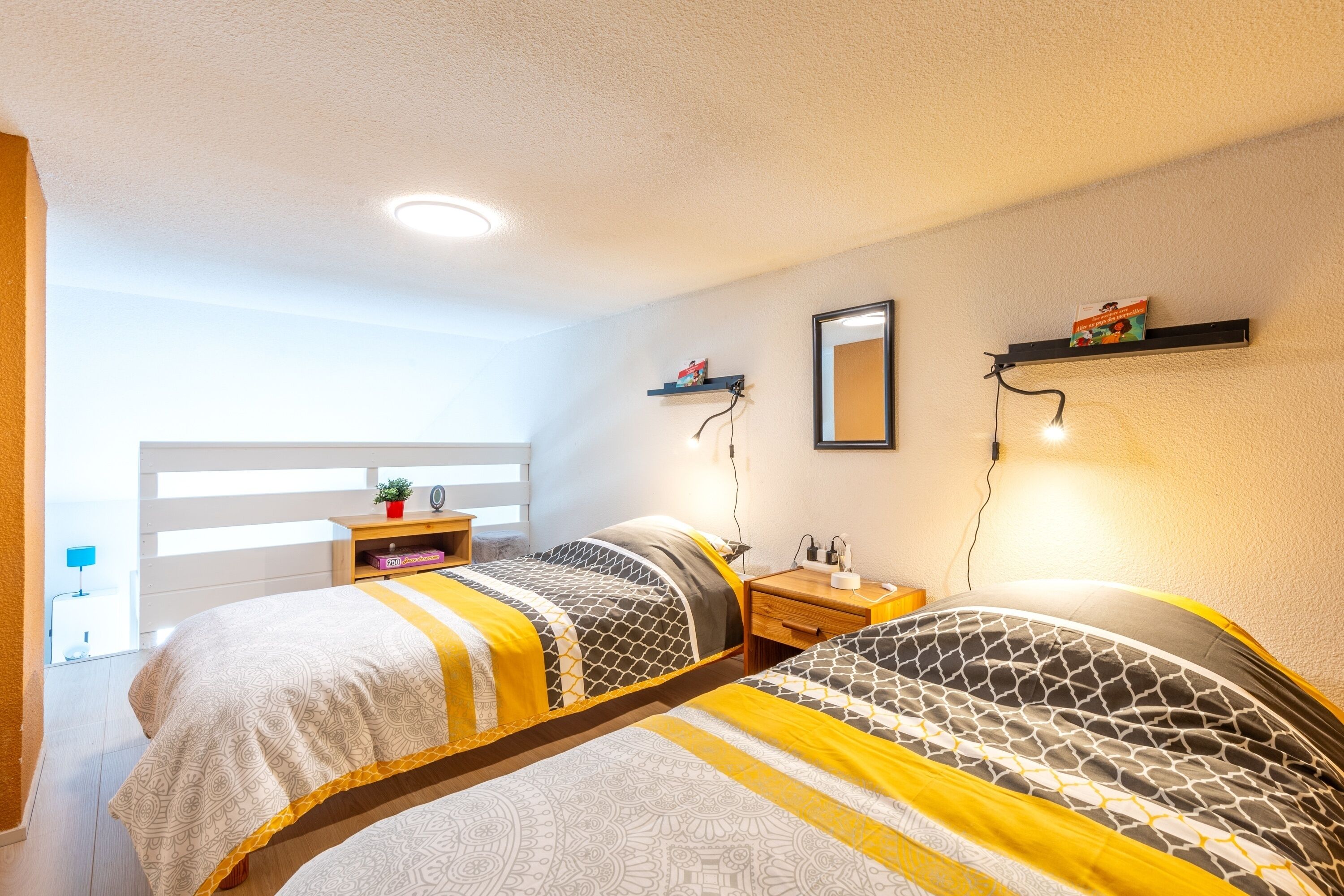 Un dormitorio con dos camas, una mesita de noche, un espejo y una estantería con libros.