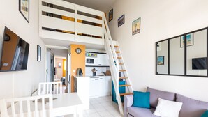 A compact living space with a dining area, sofa, kitchenette, and a staircase leading to an upper level.