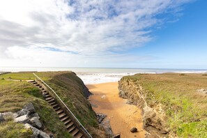 A coastal landscape with a staircase leading down to a beach, surrounded by grassy terrain and cliffs. - La Corniche d'Or - Appt à 150m de la plage (Saint-Hilaire-de-Riez)
