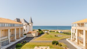 A coastal hotel with a view of the sea, featuring a courtyard with a lawn and a pathway leading to the beach.