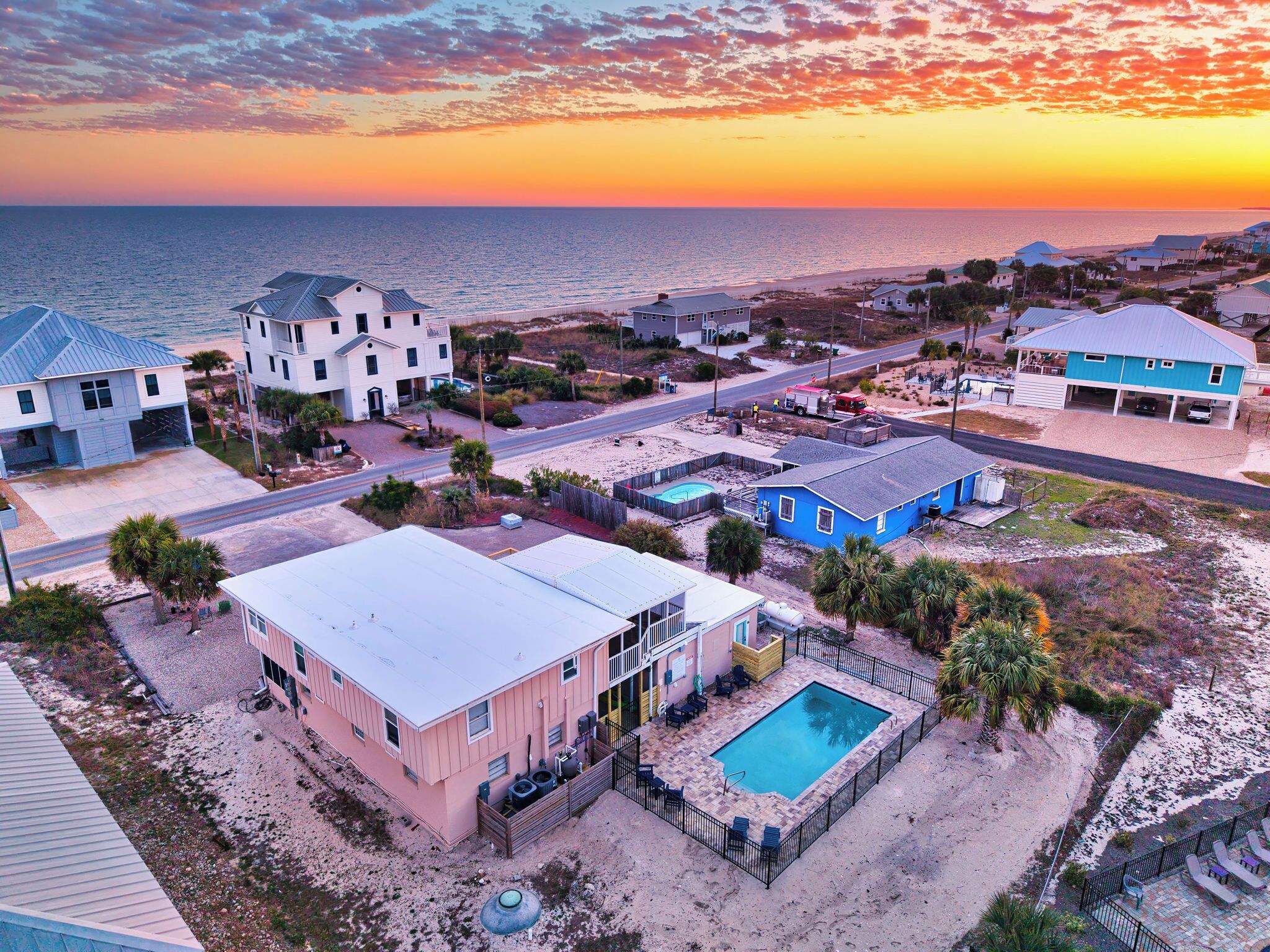 Un quartier résidentiel en bord de mer, avec des maisons, une piscine et une plage en arrière-plan.