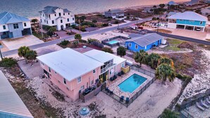 A coastal residential area with houses, a swimming pool, and a beach in the background.