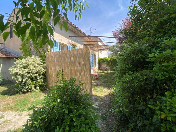 A garden with a wooden fence, a pathway, and a building with blue shutters.
