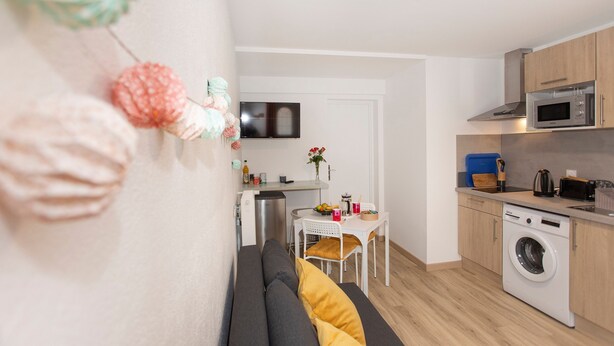 A compact kitchen with a washing machine, a microwave, and a dining area with a table and chairs.