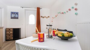 A kitchen with a white table, a fruit bowl, a coffee maker, and a potted plant.