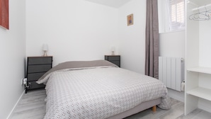 A bedroom with a bed, two bedside tables, a radiator, and a window with curtains.