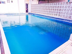 A swimming pool with clear blue water, surrounded by a tiled deck and a decorative wall with a geometric pattern.