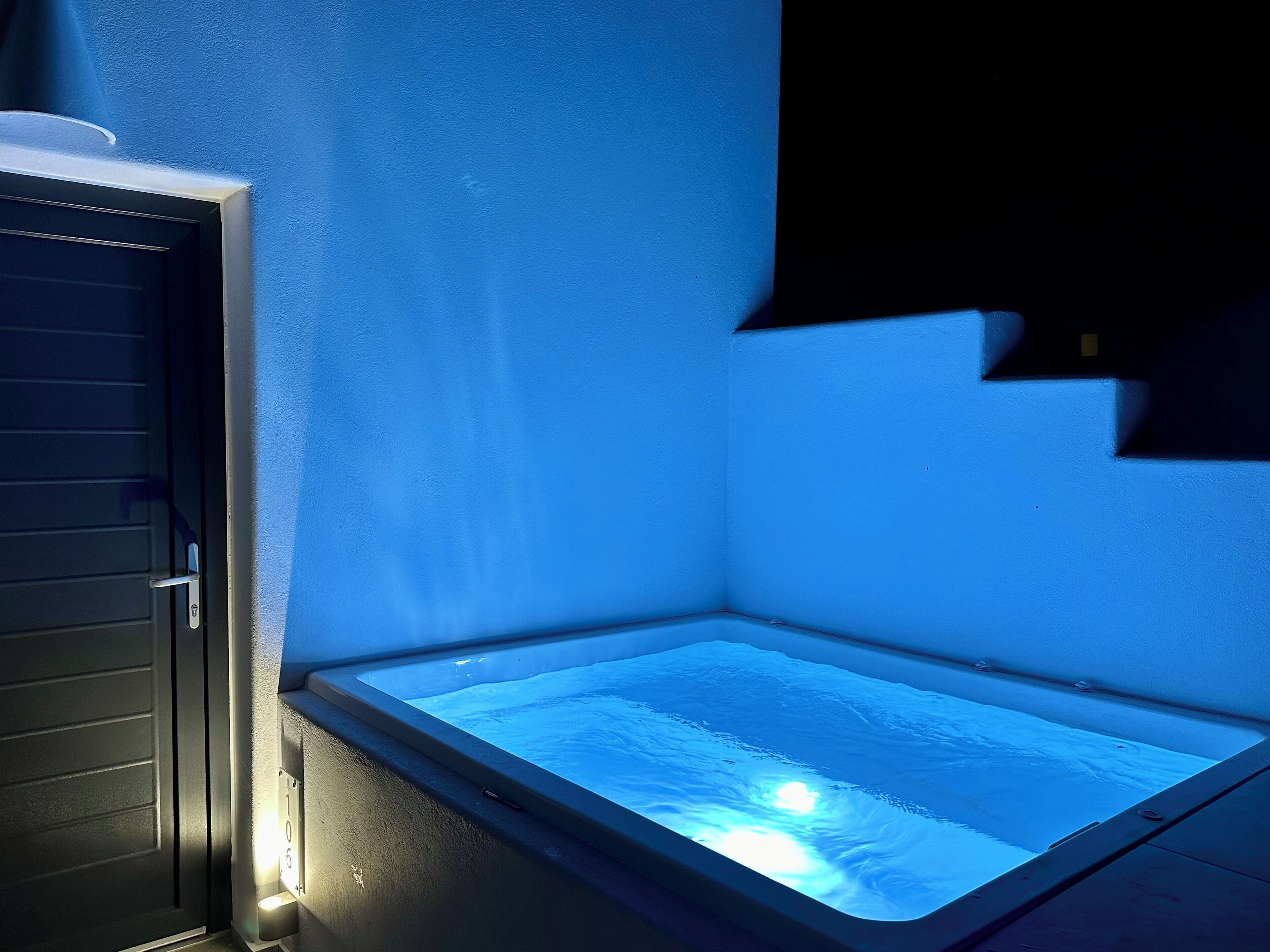 Una esquina de habitación con una bañera debajo de una ventana, una puerta y una pared azul.