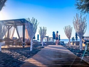 Une promenade en bord de mer avec une terrasse en bois, des chaises de plage et des parasols.