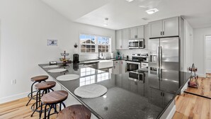 A modern kitchen with a central island, stainless steel appliances, and a large window providing natural light. - BLUEBERRY COTTAGE is located in Mena.  WIFI, remodeled , Lockable bike storage ! (Mena)