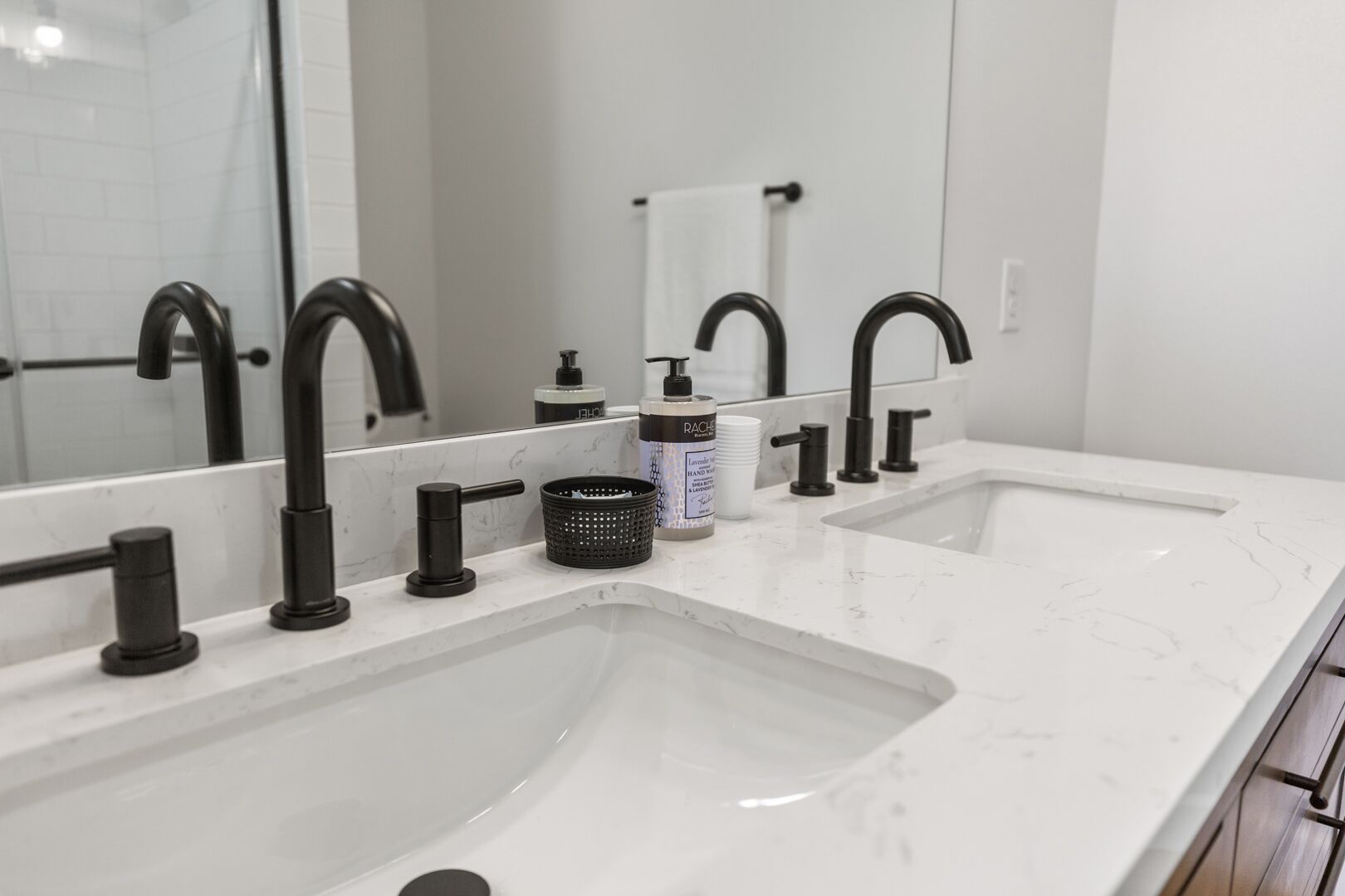 Un baño moderno con dos lavamanos, grifos negros, un espejo grande y una encimera de mármol blanco.