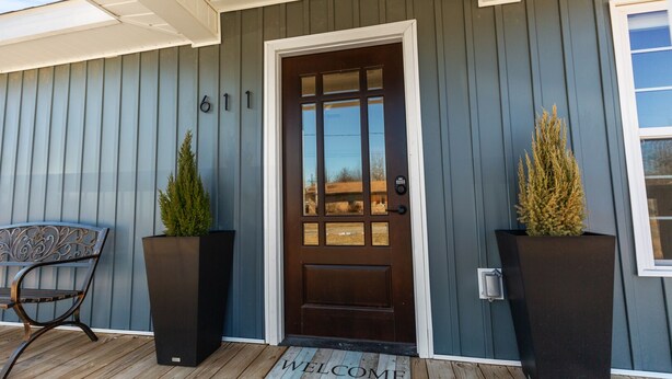 A house with a dark brown front door, a welcome mat, and two large planters on the porch. - BLUEBERRY COTTAGE is located in Mena.  WIFI, remodeled , Lockable bike storage ! (Mena)