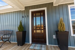 A house with a dark brown front door, a welcome mat, and two large planters on the porch. - BLUEBERRY COTTAGE is located in Mena.  WIFI, remodeled , Lockable bike storage ! (Mena)