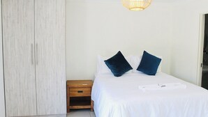 A bedroom with a bed, two pillows, a bedside table, a wardrobe, and a hanging light fixture. - Splendid 1-bed Apartment in Sandton (Johannesburg)