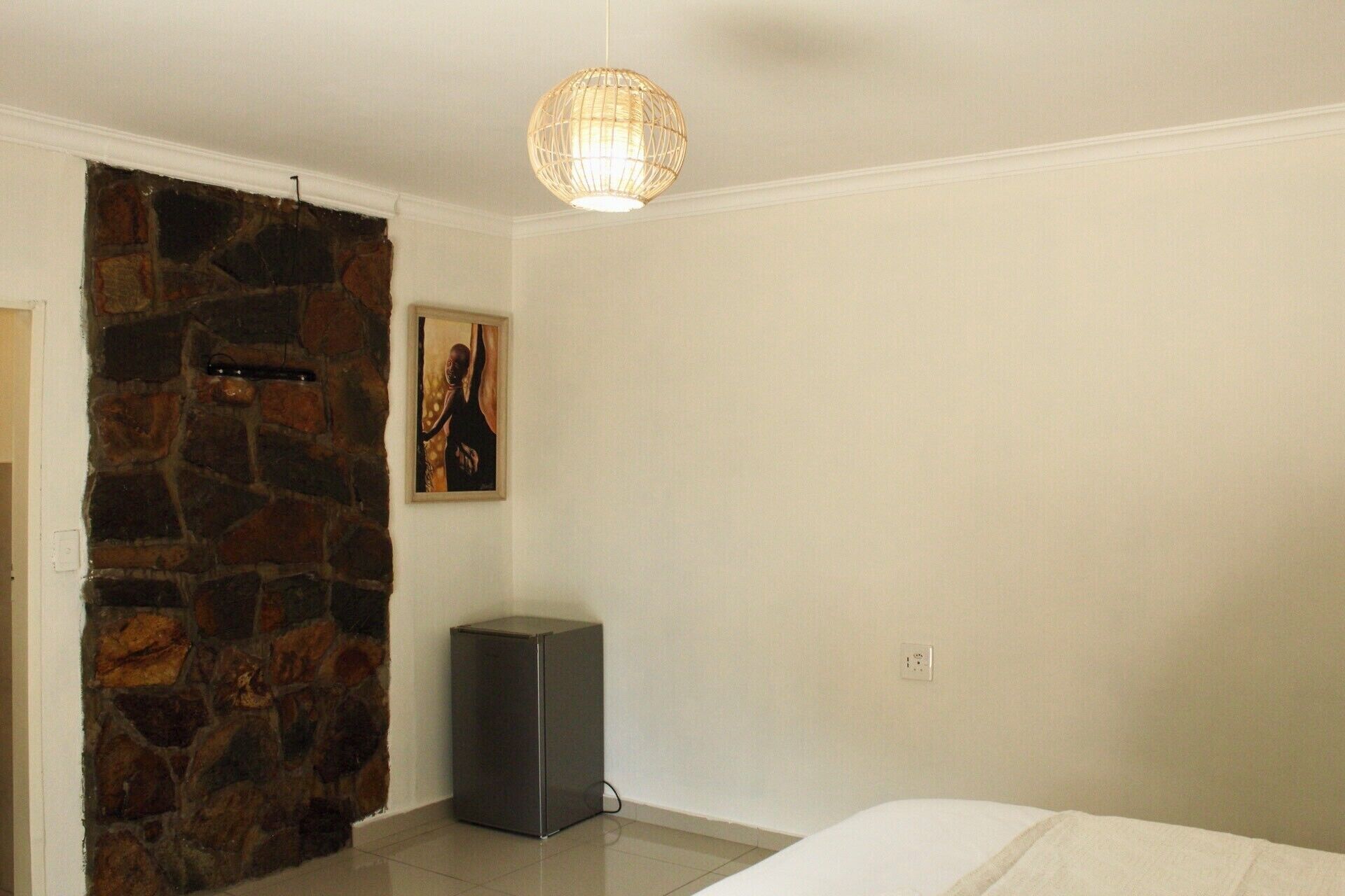 A bedroom with a stone wall, a painting, a small speaker, and a bed.