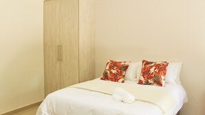 A hotel room with a bed, a wardrobe, and a hanging light fixture. - Charming 1-bed Apartment in Sandton (Johannesburg)