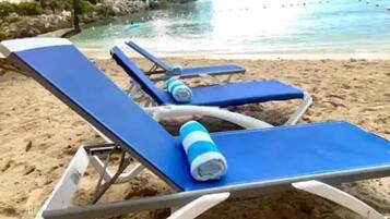 Een strand met blauwe ligstoelen en een blauwe handdoek.