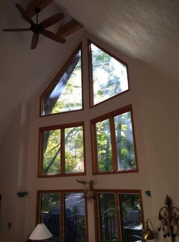 A room with a sloped ceiling, a ceiling fan, and multiple windows offering views of greenery. - Harbor Springs Vacation Rental-Thanksgiving open now (Harbor Springs)