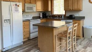 Eine kompakte Küche mit Holzausbau, einer zentralen Kochinsel inklusive Barhocker, einem Kühlschrank, einer Mikrowelle und einem Herd.