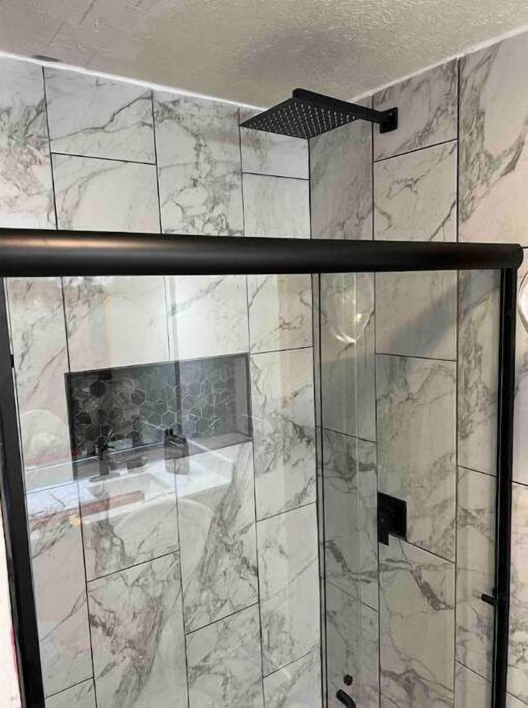 A modern bathroom with marble tiles, a glass shower enclosure, and a black showerhead.