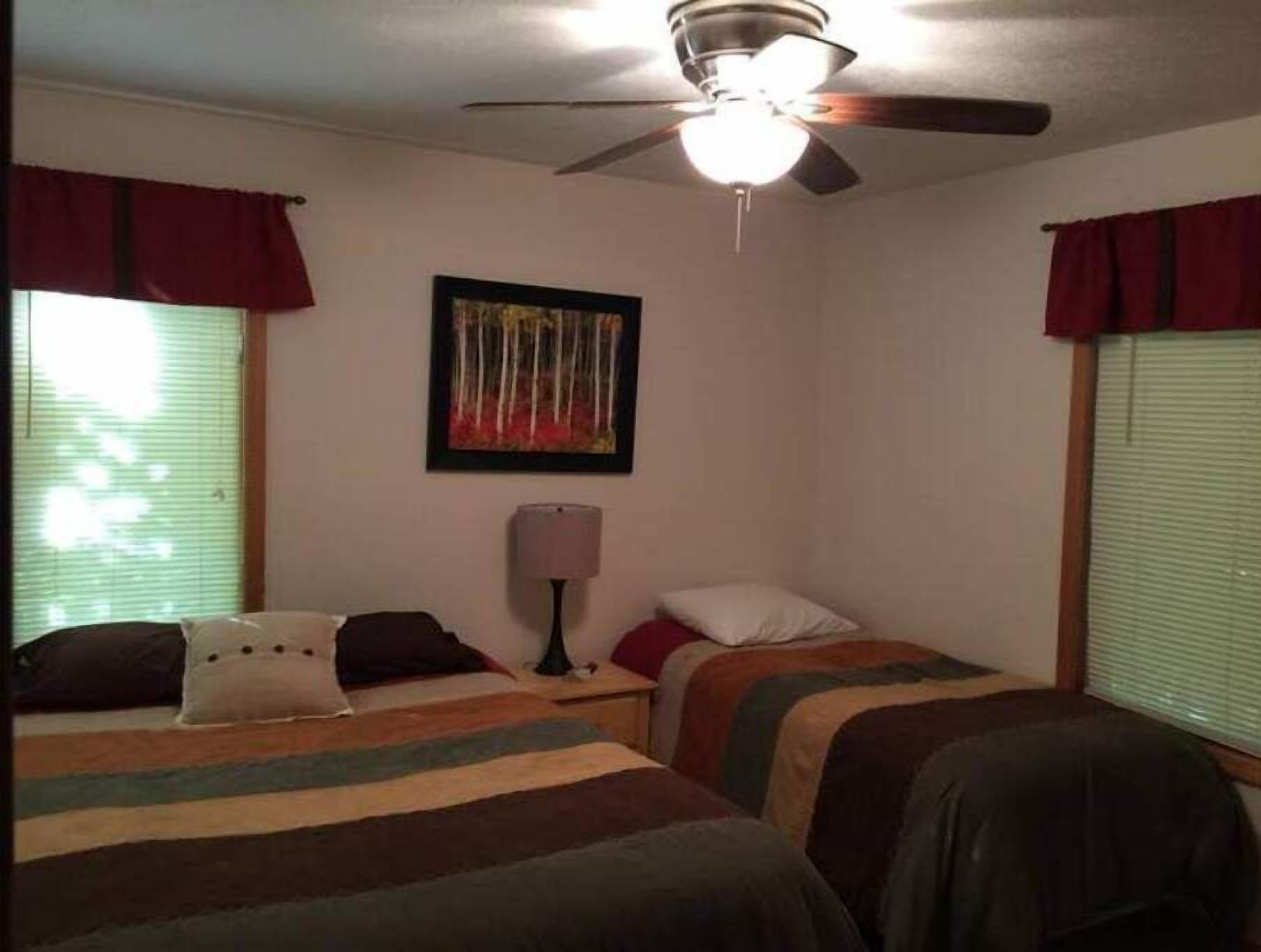 A bedroom with two beds, a ceiling fan, a nightstand with a lamp, and a painting on the wall.