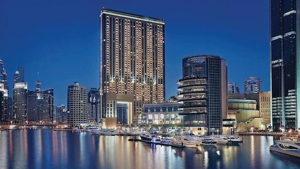A high-rise building with a modern design, situated near a marina with boats docked. - The Address Dubai Marina 1BR (Dubai)