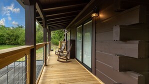 Eine Holzterrasse mit Geländer, einem Schaukelstuhl und einer Glastür zu einem überdachten Bereich.
