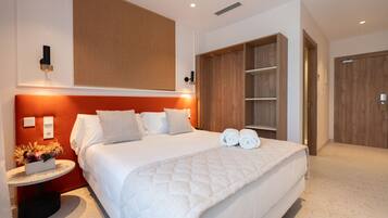 A modern hotel room with a large bed, a wooden wardrobe, and a small table with a flower arrangement.